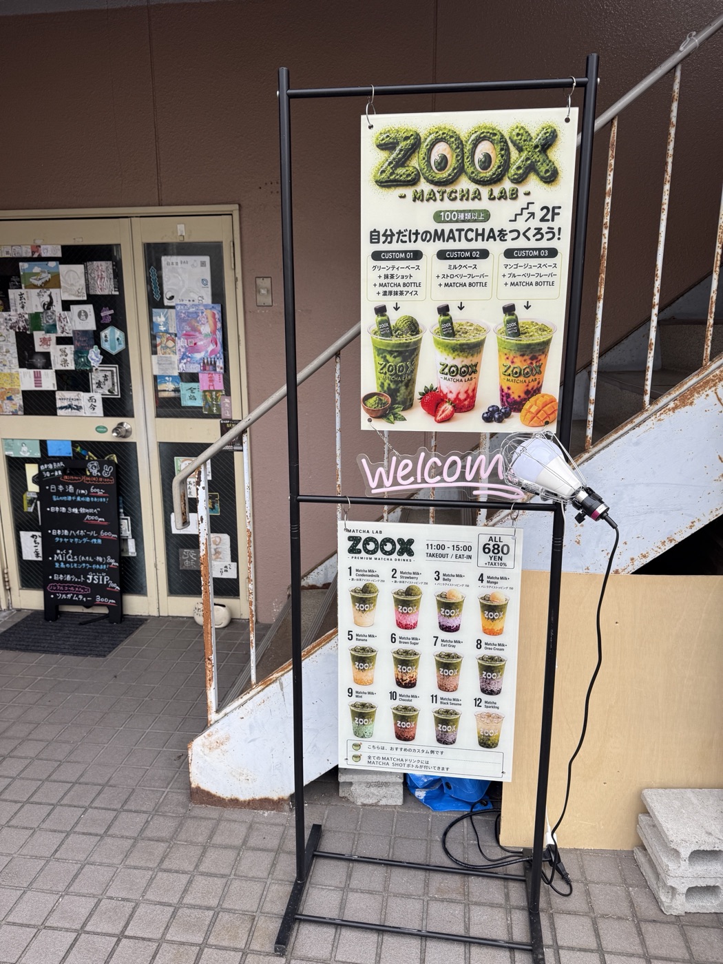 階段の前に立つZOOXの看板