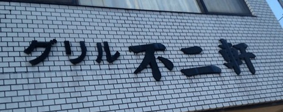 白いタイルの壁に黒い文字「グリル 不二軒」